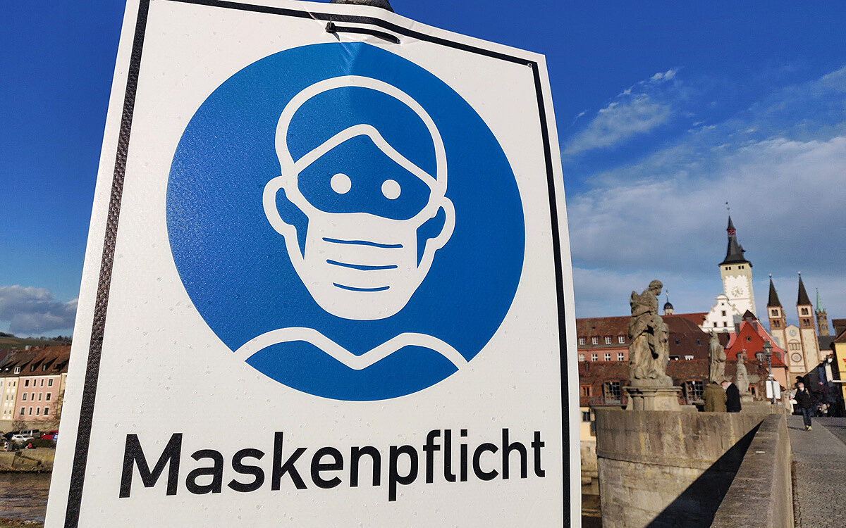 Maskenpflicht steht groß auf einem Schild auf Alte Mainbrücke im Hintergrund ist Würzburg Maskenpflicht steht groß auf einem Schild auf Alte Mainbrücke im Hintergrund ist Würzburg